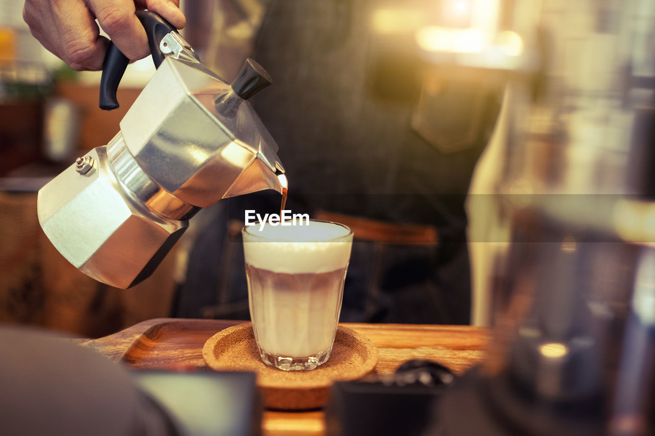 Midsection of barista pouring cream in coffee at cafe