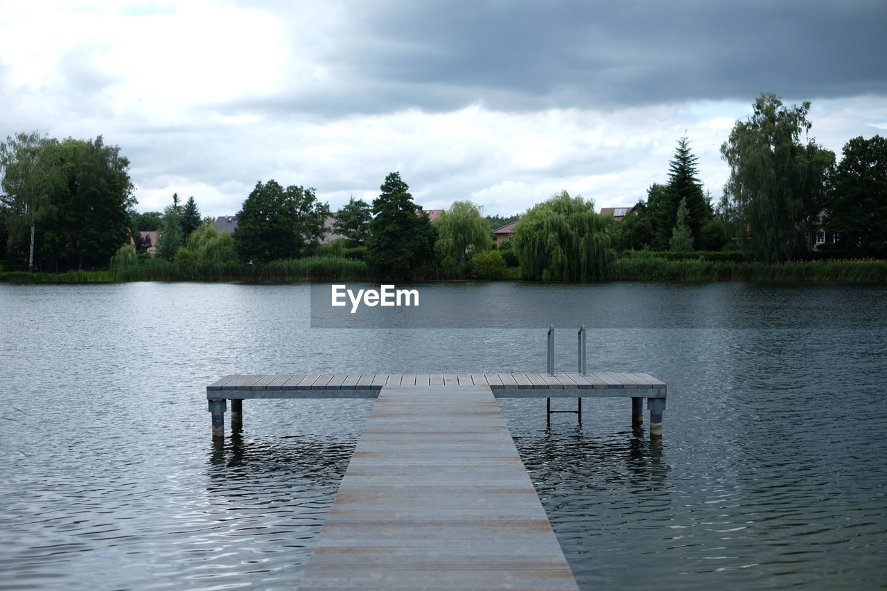 Empty jetty at lake against cloudy sky