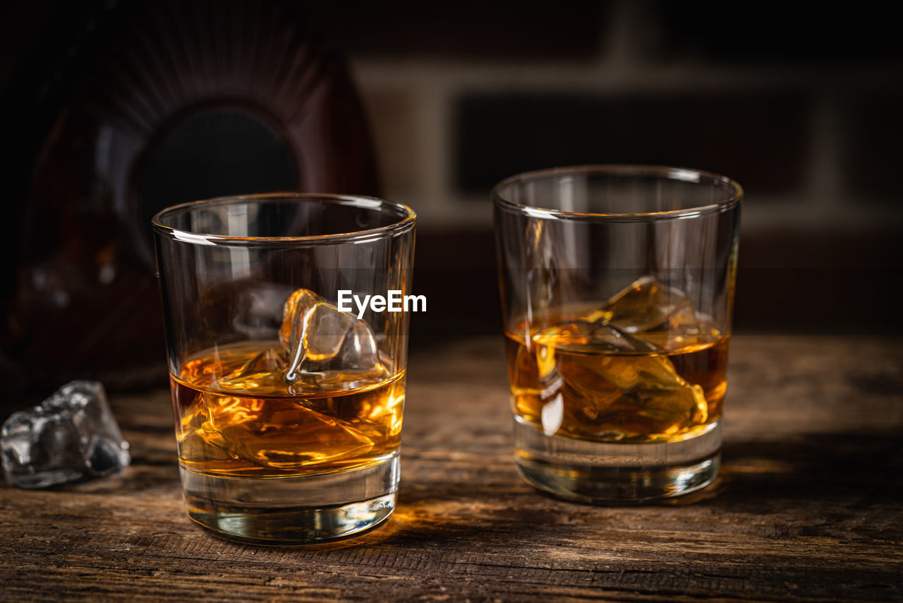 whisky, glass, drinking glass, household equipment, old fashioned glass, drink, food and drink, distilled beverage, refreshment, whiskey, alcoholic beverage, alcohol, shot glass, table, indoors, wood, no people, lighting, bar, close-up, focus on foreground, relaxation, beer