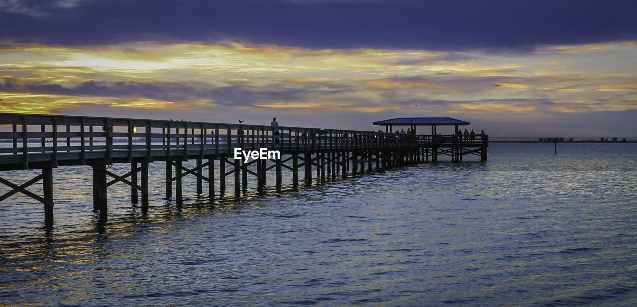 Pier over calm sea against cloudy sky