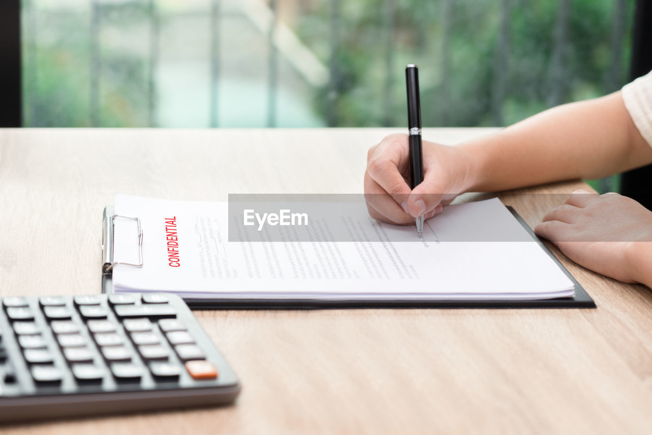 Cropped hand of businesswoman signing contract on table in office