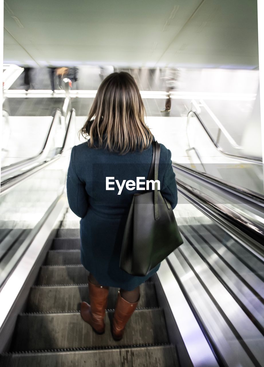 REAR VIEW OF WOMAN ON ESCALATOR IN SUBWAY