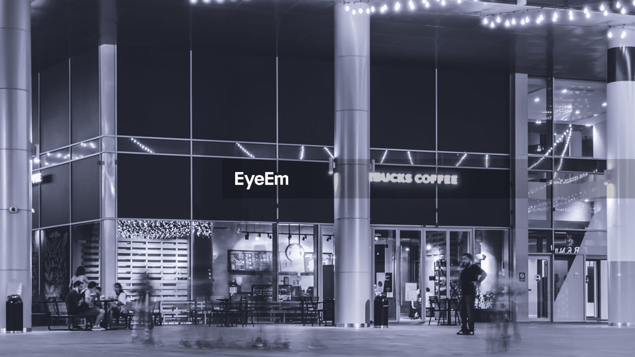 PEOPLE WALKING ON ILLUMINATED MODERN BUILDING