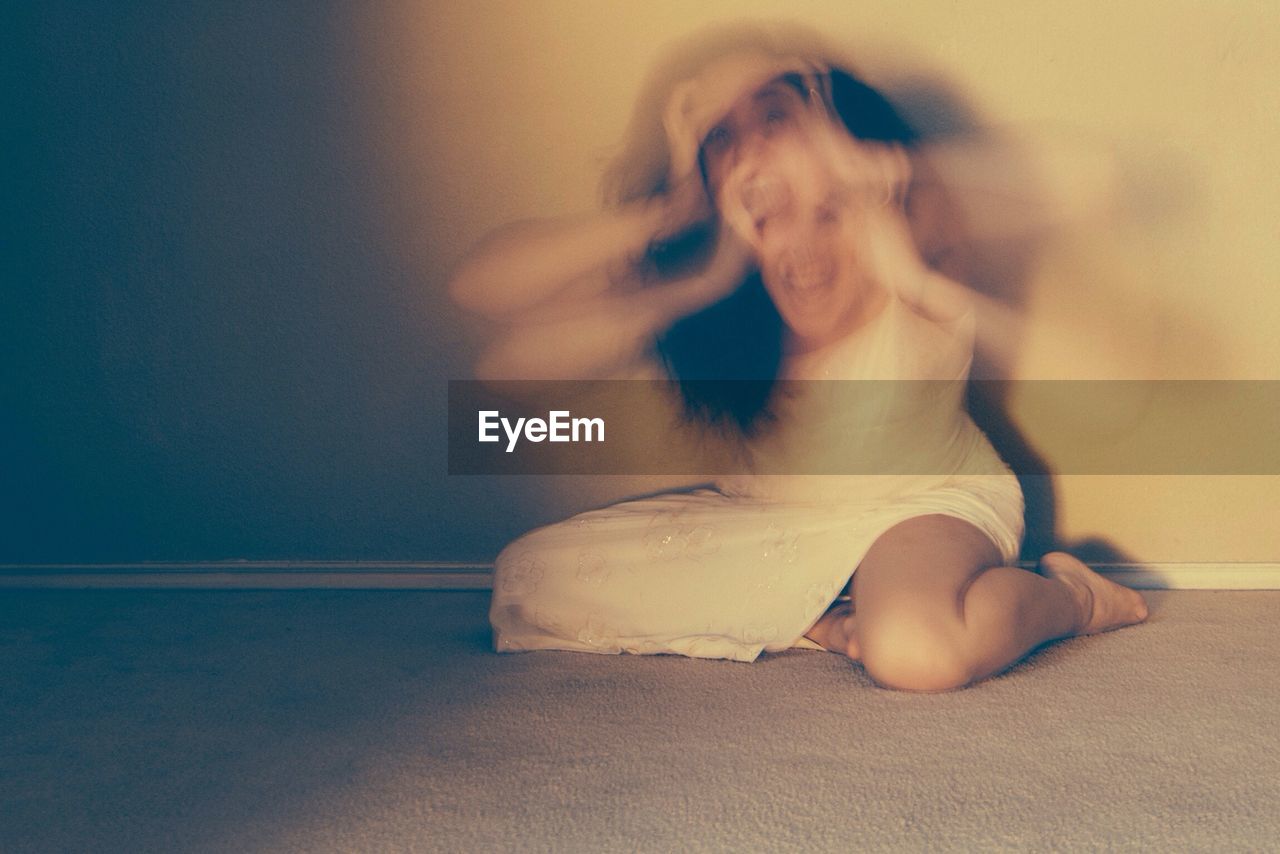 Blurred motion of woman screaming with holding head against wall