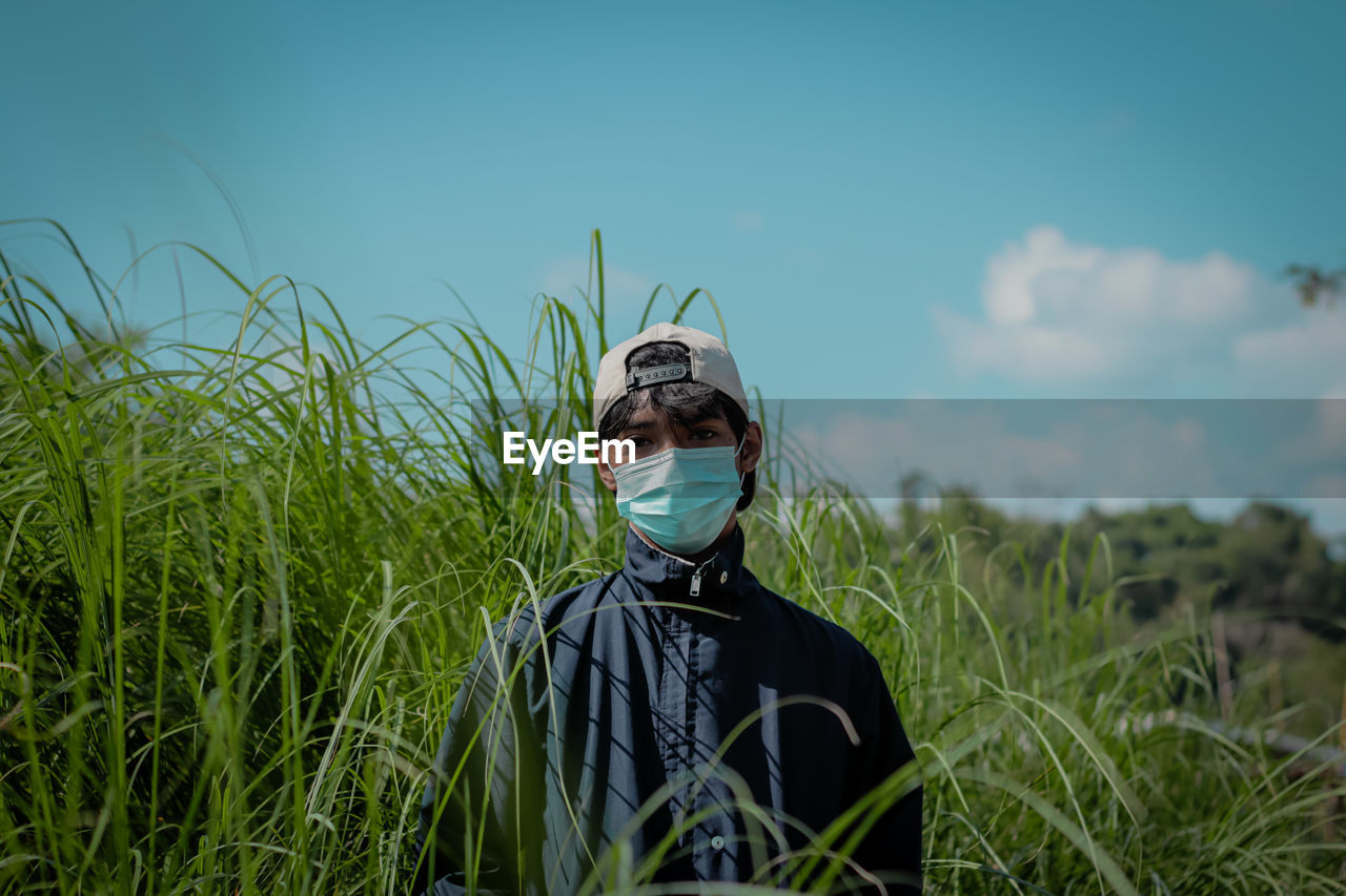 Rear view of man standing against sky and tall grass. 