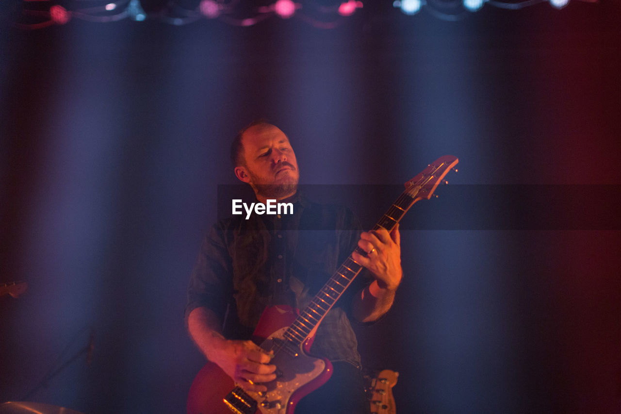 MIDSECTION OF MAN PLAYING GUITAR AT MUSIC CONCERT