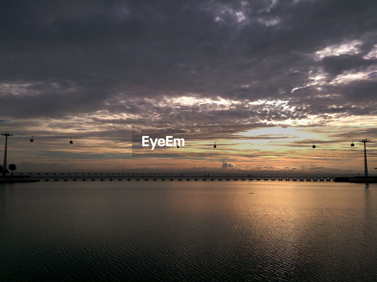 Overhead cable cars over river against cloudy sky at sunset