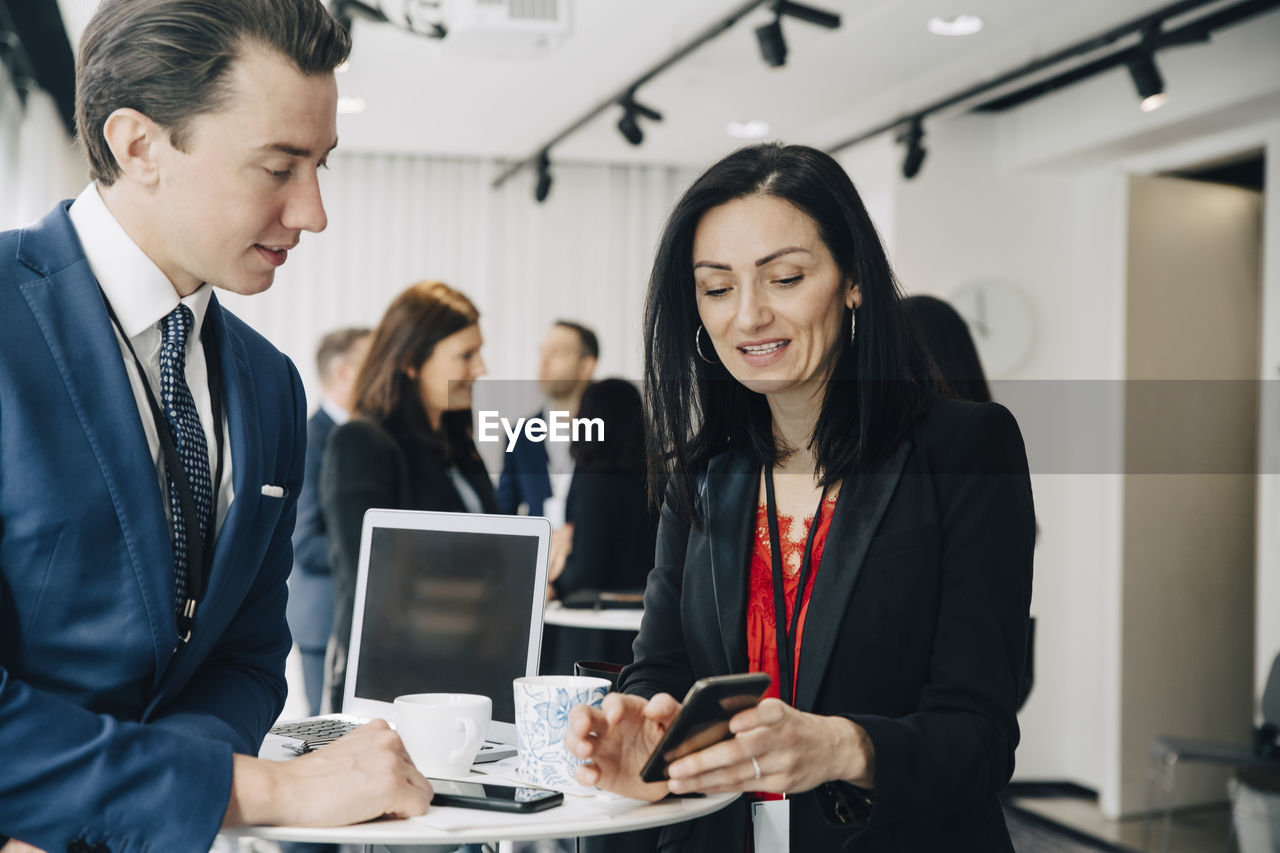 Female coworker showing smart phone to entrepreneur at office seminar