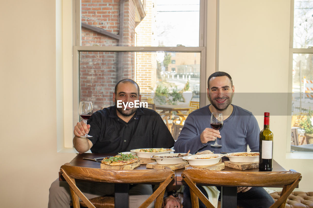 Two proud business owners sit together at a restaurant table with wine