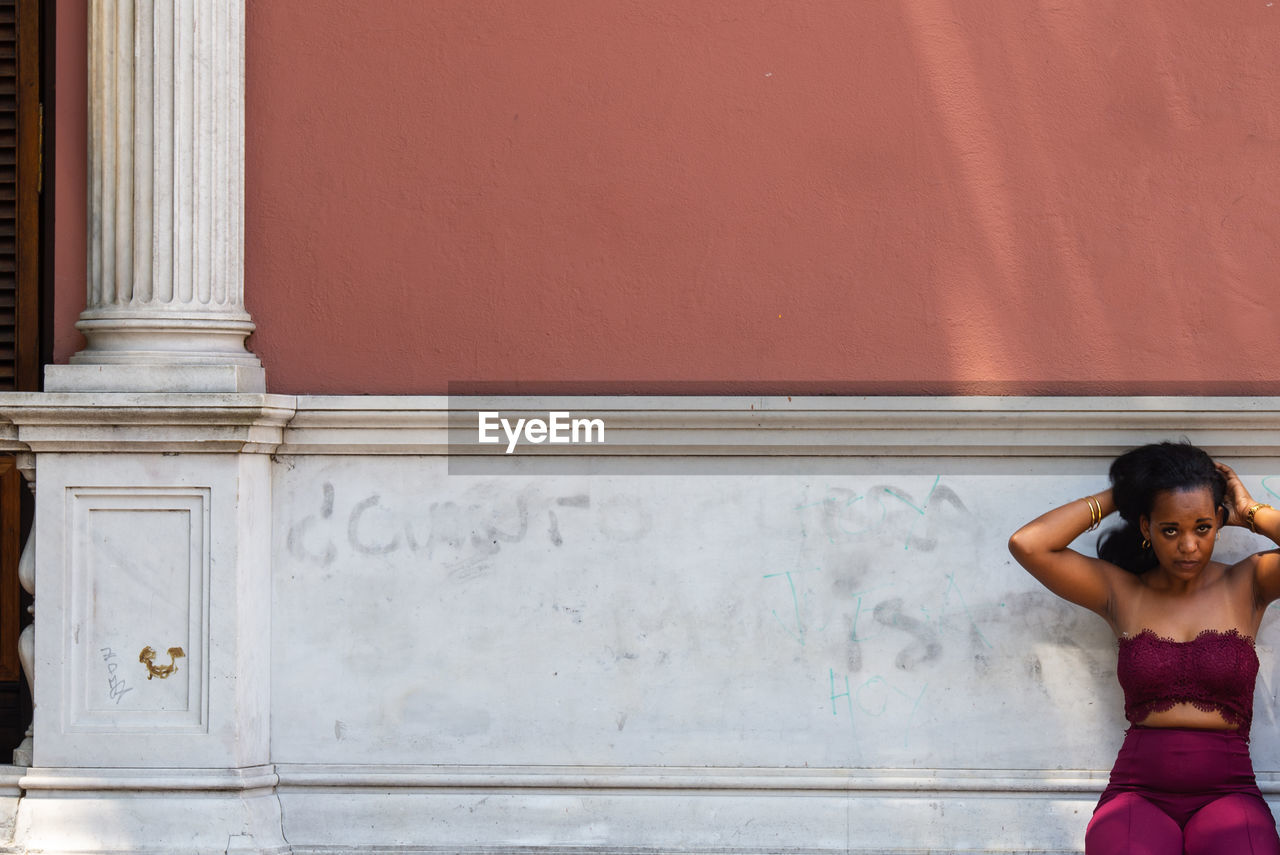 PORTRAIT OF A YOUNG WOMAN STANDING AGAINST WALL