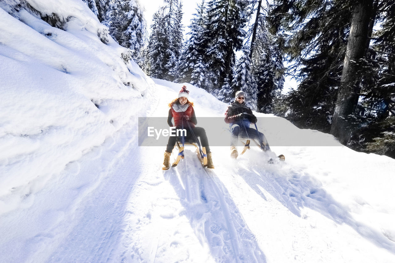 Couple sledding on snow during sunny day in winter