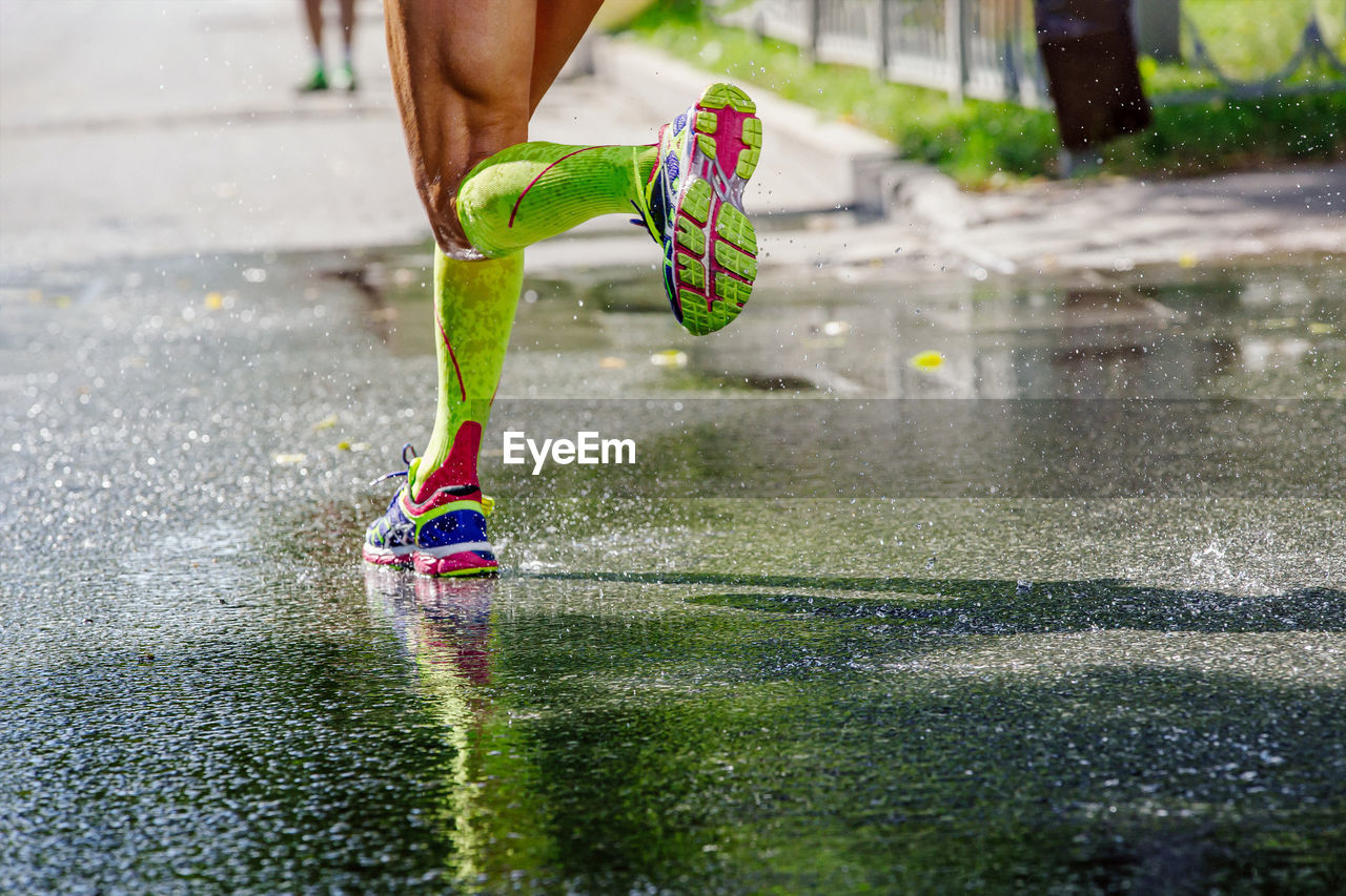 low section of woman jumping on puddle