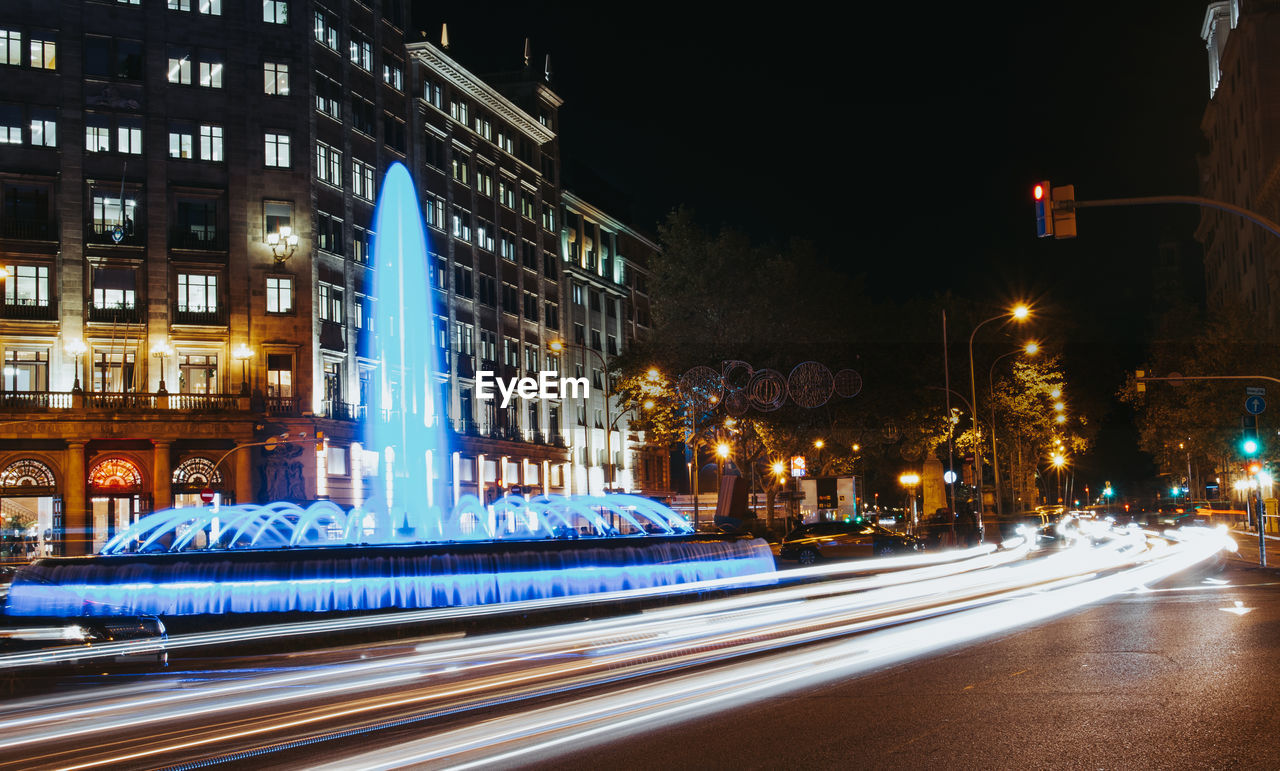 Light trails on city street by buildings at night