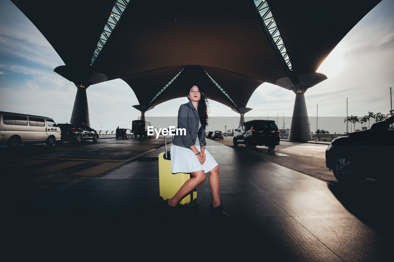 Woman sitting on luggage underneath bridge