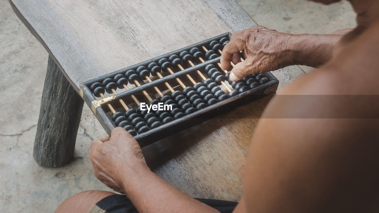 Midsection of shirtless man playing with abacus