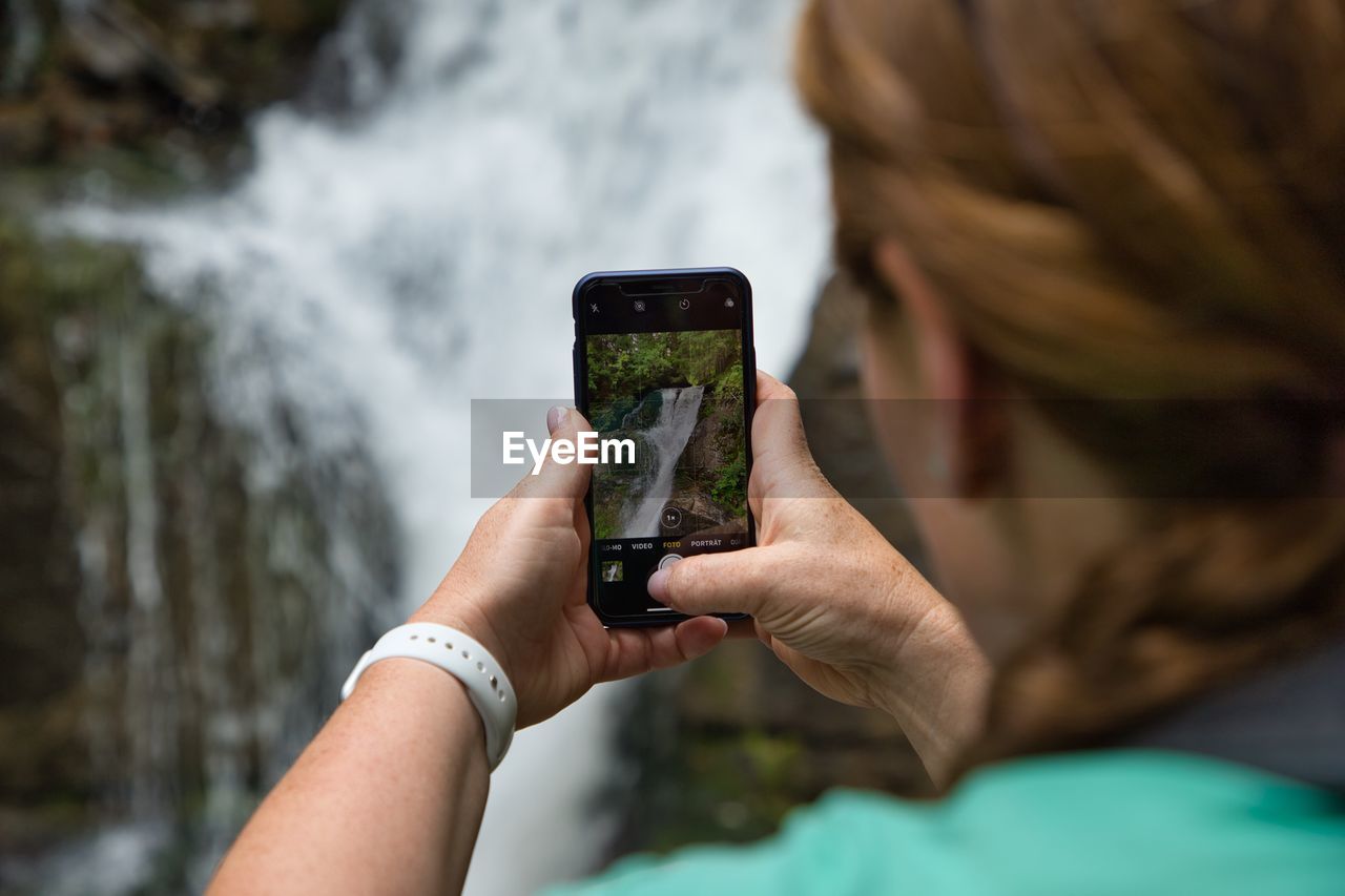 Close-up of woman photographing waterfall with smart phone