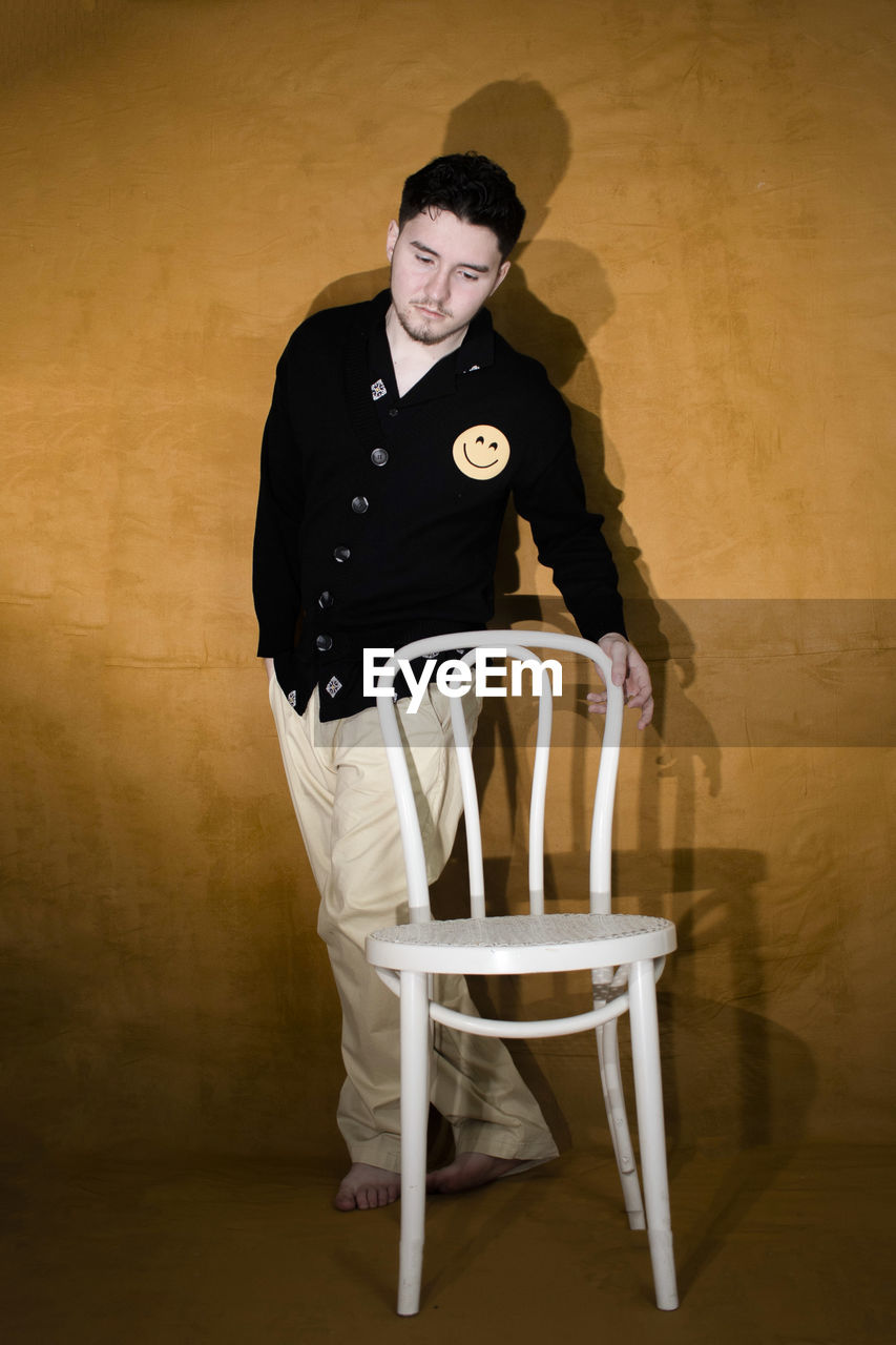 one person, chair, portrait, clothing, adult, seat, indoors, sitting, furniture, looking at camera, full length, studio shot, men, hat, person, emotion, standing