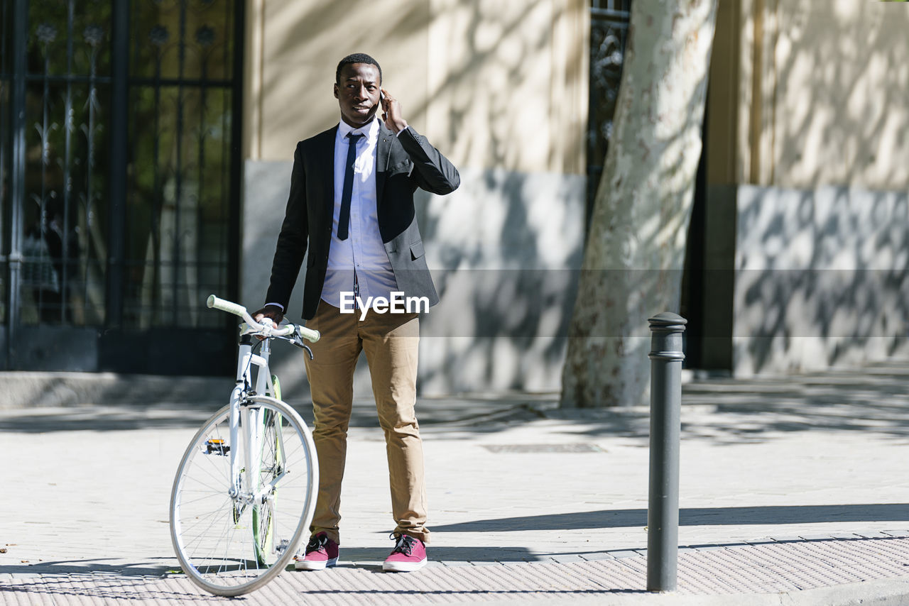 Businessman with bicycle talking on smart phone in city