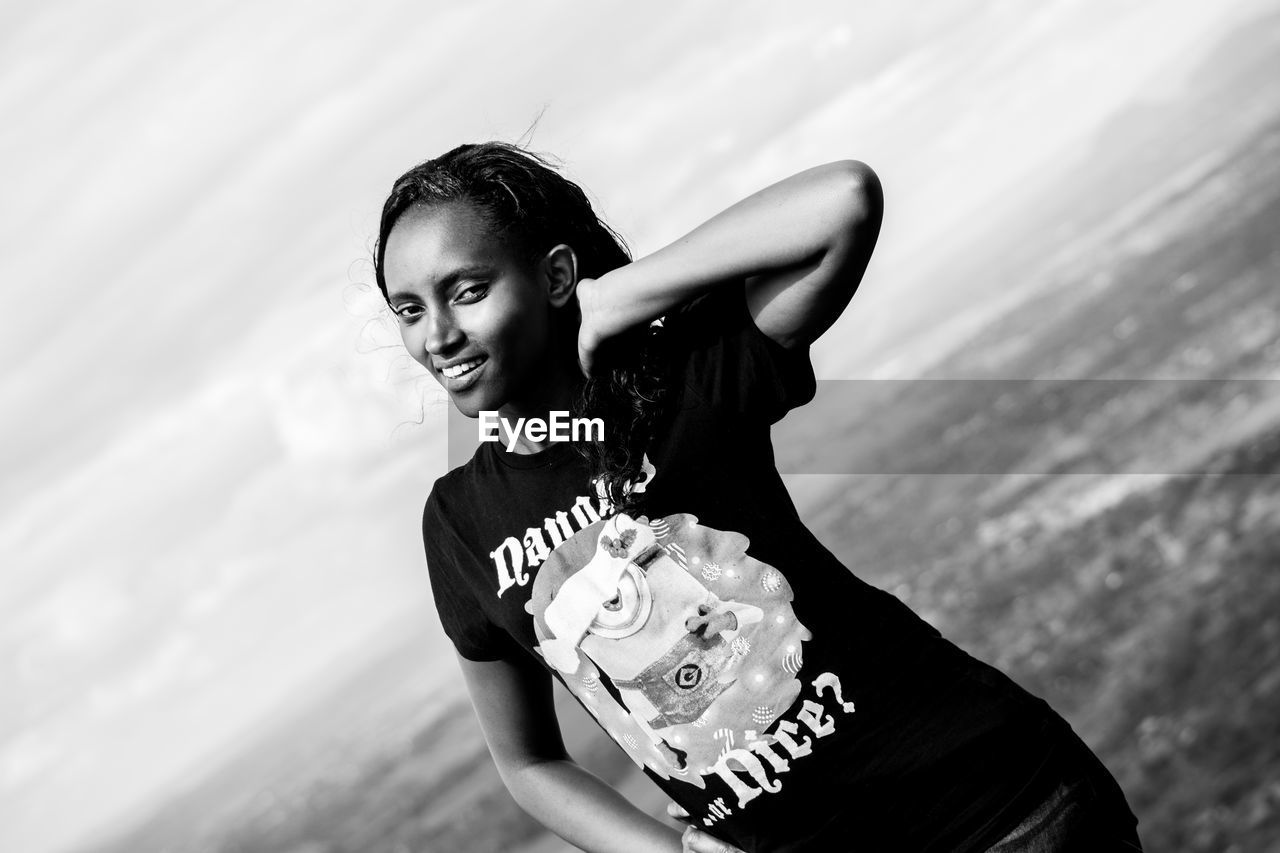 Portrait of smiling young adult standing against cloudy sky