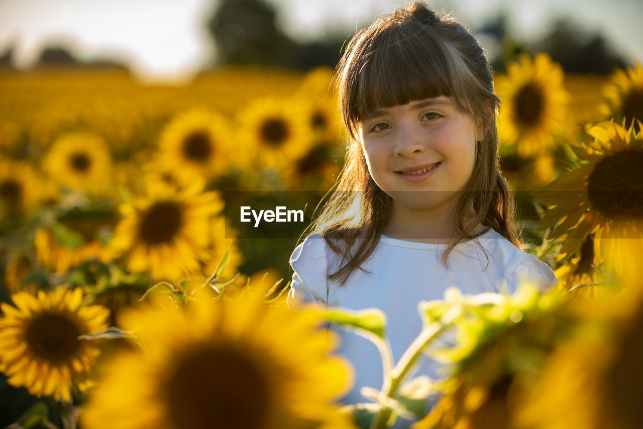 PORTRAIT OF SMILING GIRL WITH SUNFLOWER AT PARK