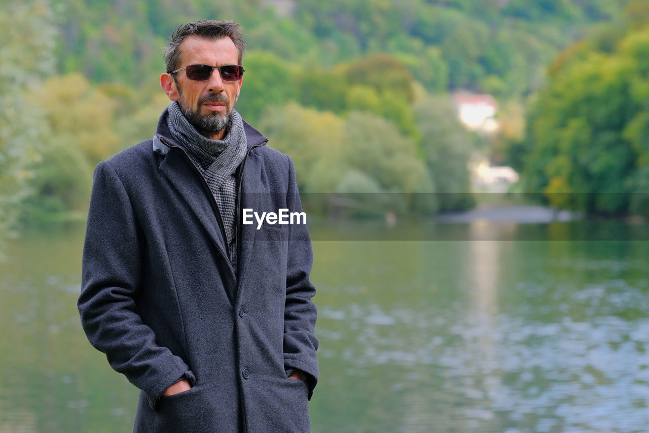 Portrait of young man wearing sunglasses standing by lake