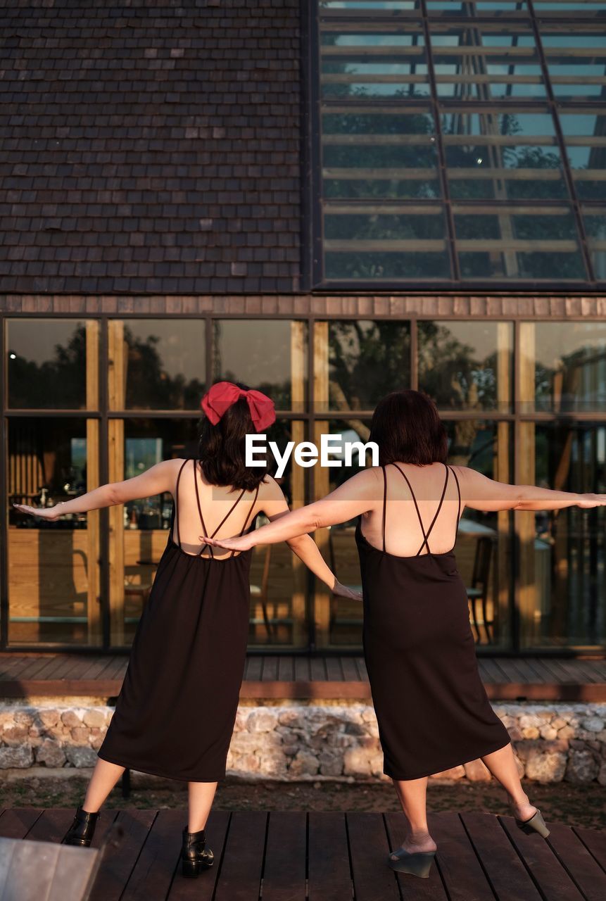 Portrait of 2 women in black backless dress against building