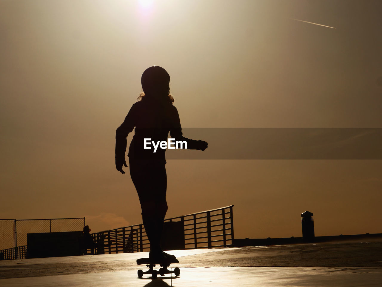 Silhouette woman skateboarding on footpath against sky during sunset