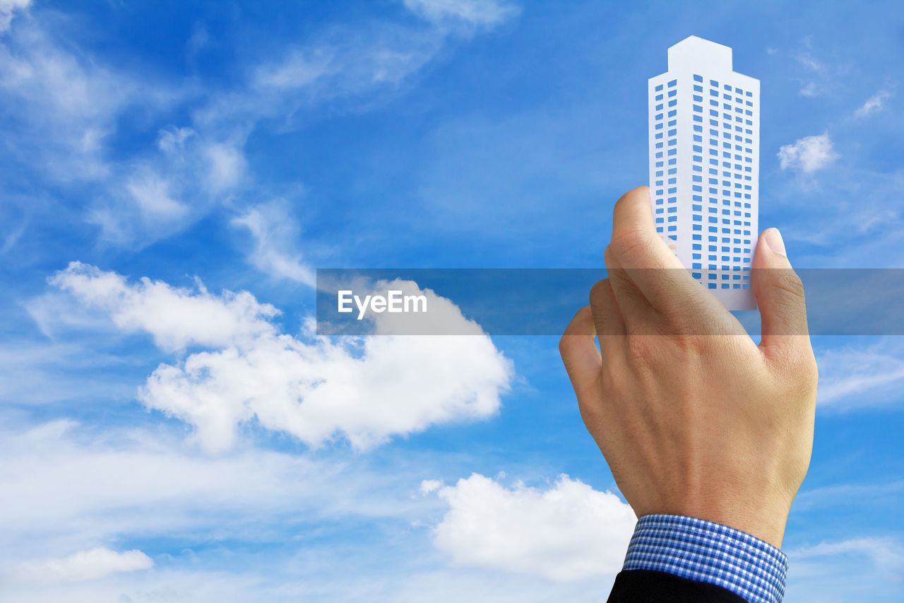 Cropped of business person holding model building against cloudy sky