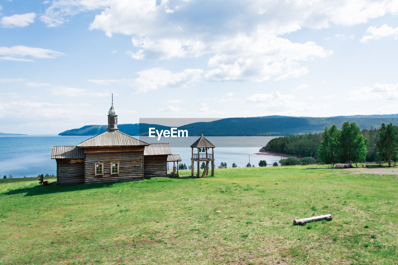 An old wooden russian house with a bell tower on the river bank on a summer day