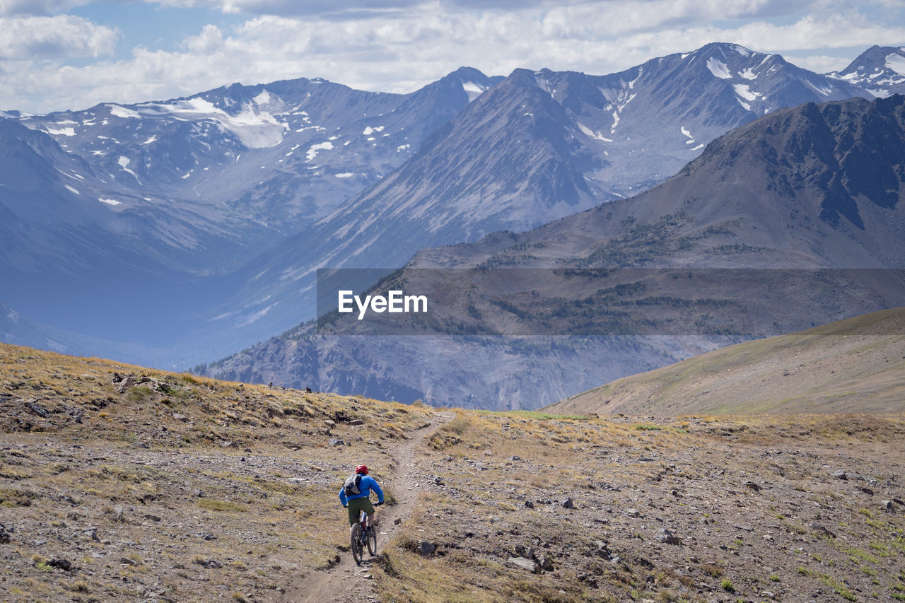 REAR VIEW OF MAN WALKING ON MOUNTAINS