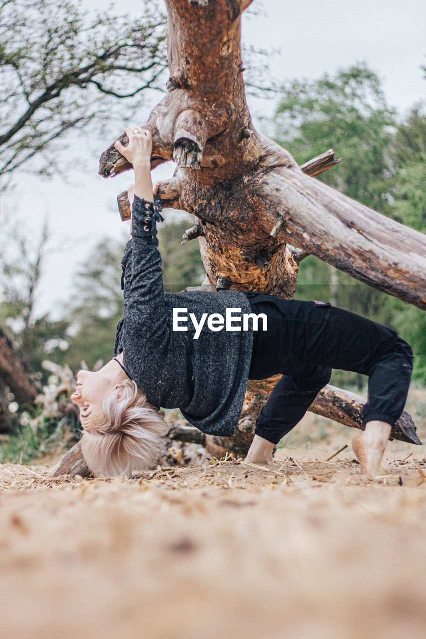 Full length of woman hanging on fallen tree at forest