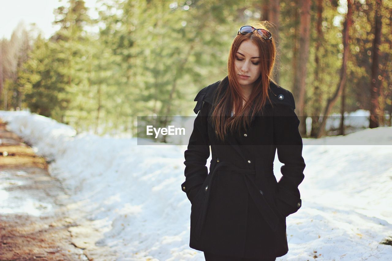 Thoughtful woman wearing winter coat standing by snow at forest