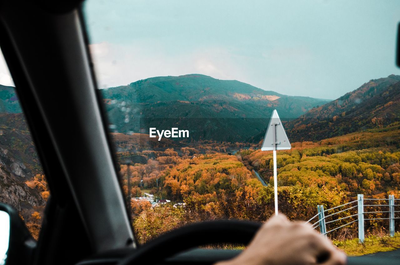 Cropped image of person driving car against mountains