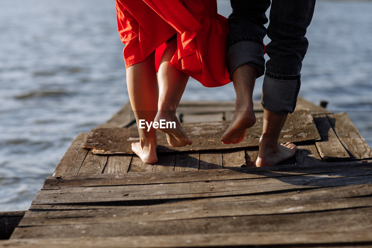 water, adult, wood, low section, human leg, pier, women, barefoot, spring, nature, dress, red, leisure activity, day, human limb, sea, limb, lifestyles, jetty, standing, clothing, holiday, two people, relaxation, beach, outdoors, shoe, summer, vacation, human foot, trip, female, fashion, men, land, sunlight, togetherness, young adult