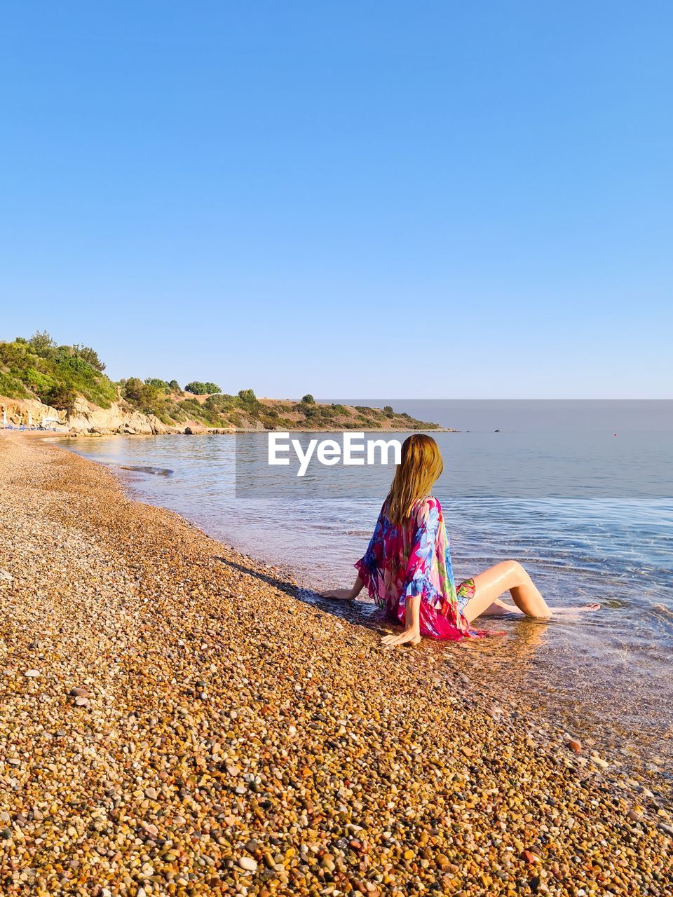 Woman sitting on pebbles at beach against clear sky