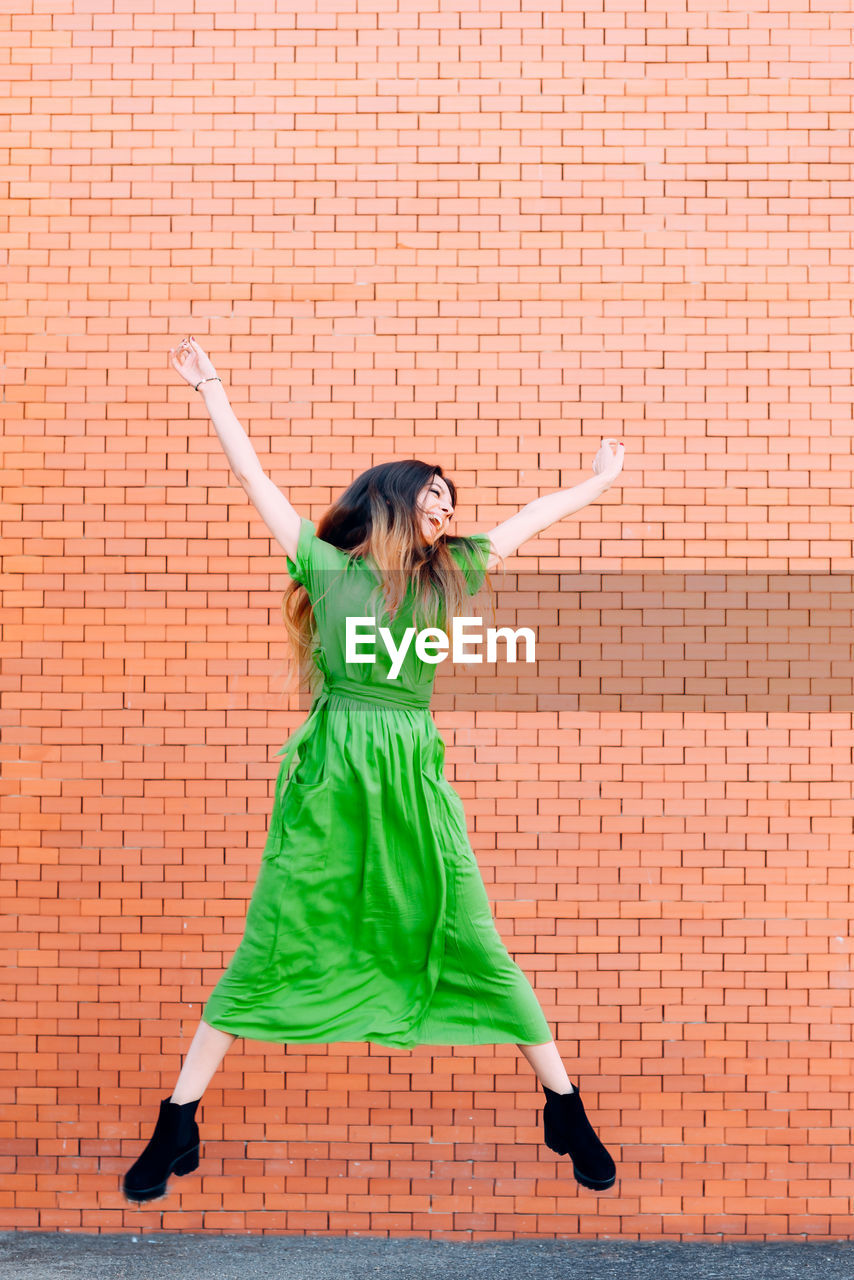 Full length of woman jumping against brick wall