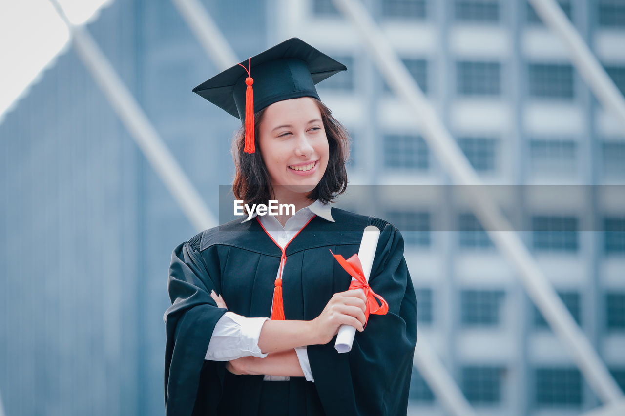 Young woman wearing graduation gown while standing against office building
