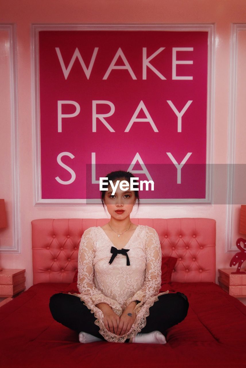 Portrait of a young attractive woman sit against wake pray slay quotes on the wall