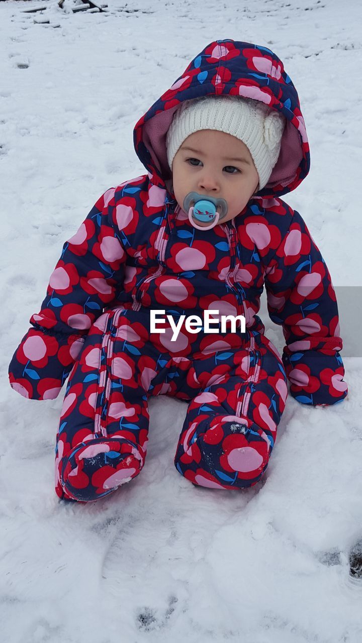 Full length of baby in warm clothing sitting on snow covered field