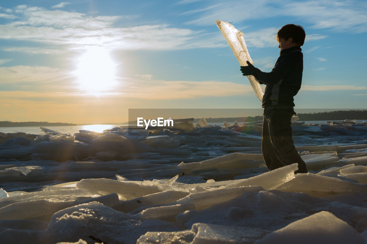 MAN STANDING ON FROZEN BEACH DURING SUNSET