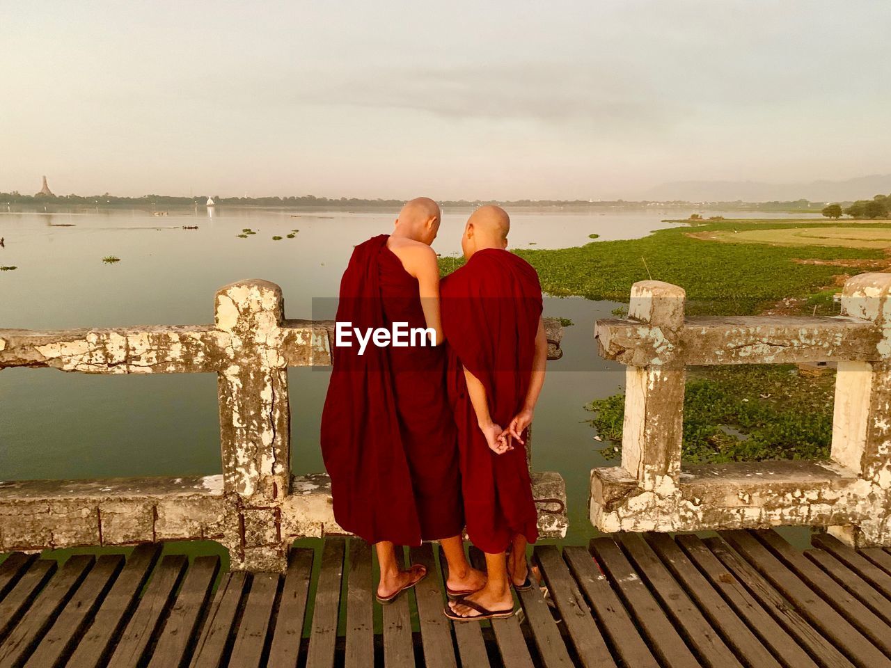 Rear view of monks standing by railing against sea and sky