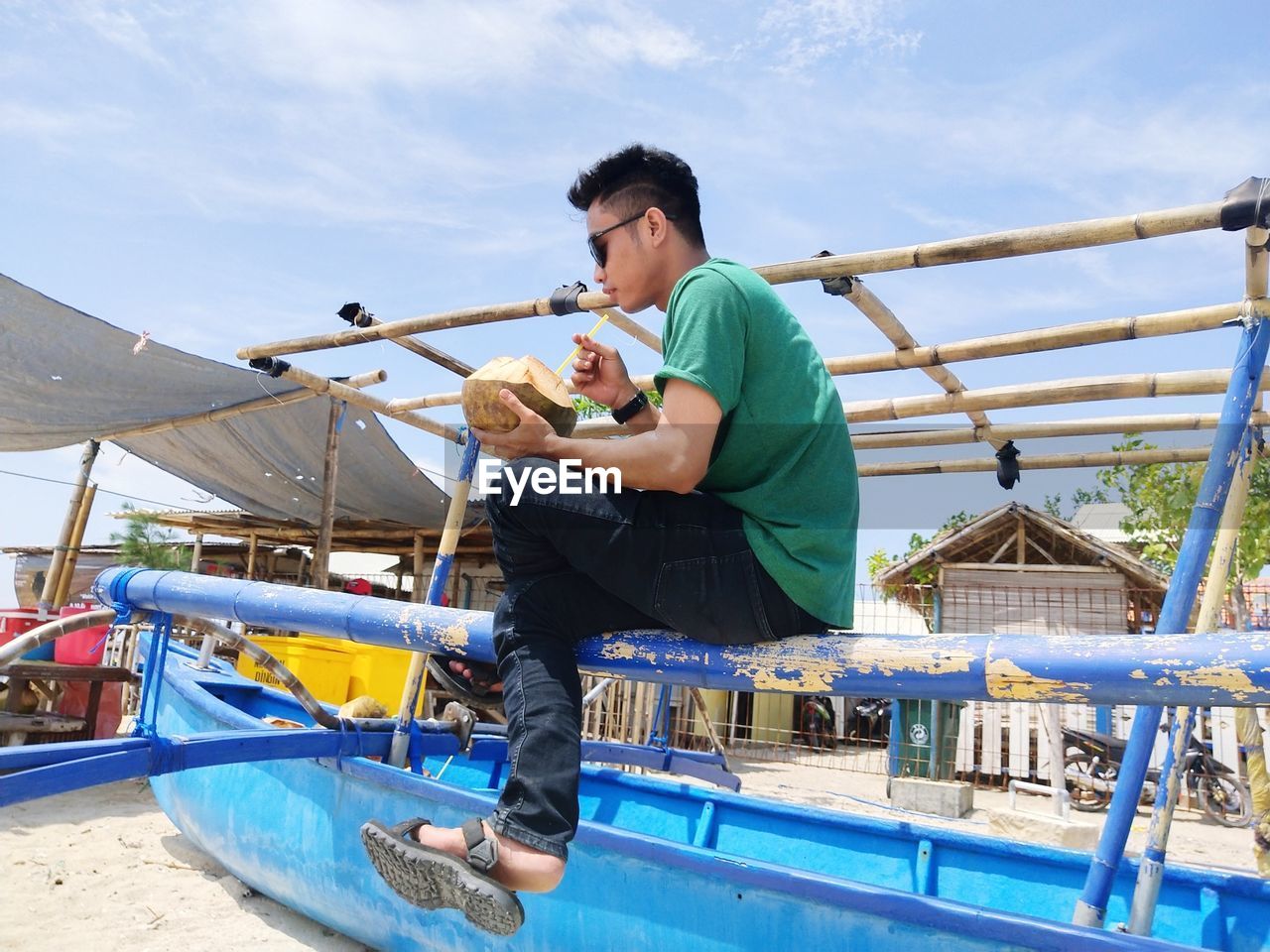 Low angle view of man drinking coconut water while sitting on nautical vessel against sky