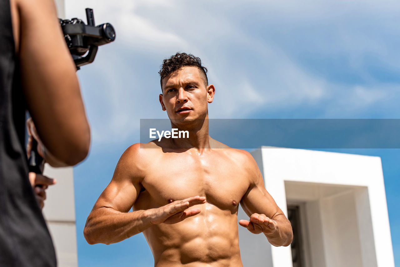 Young shirtless men exercising against sky outdoors