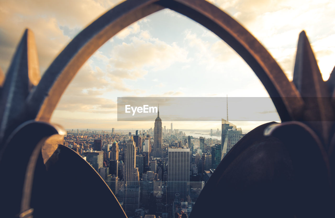 Modern buildings in city seen through arch against cloudy sky