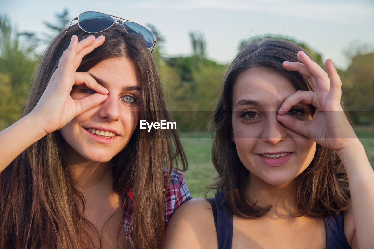 Portrait of smiling young woman gesturing ok sign against sky