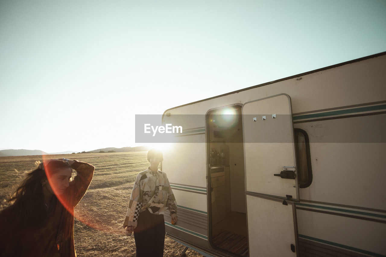 Friends standing by camper van on field during sunny day