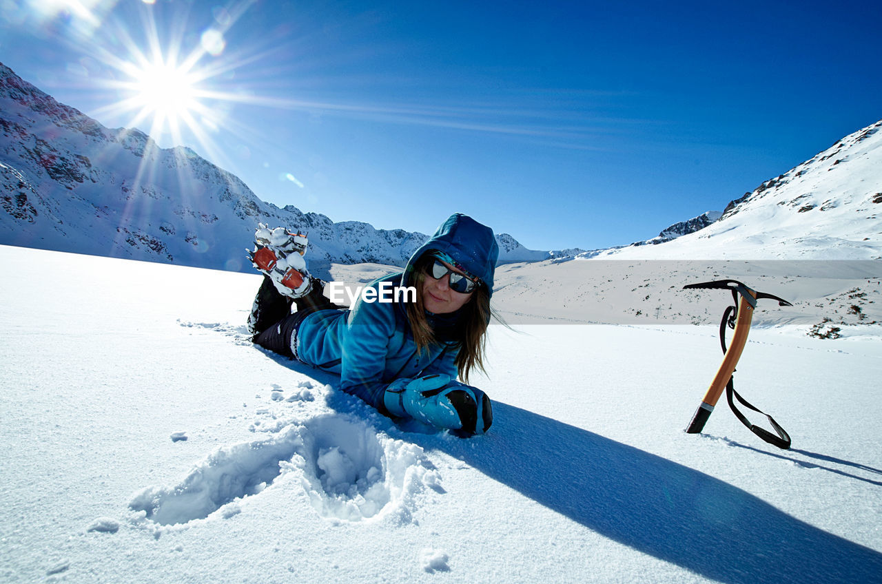 Portrait of woman lying on snowcapped mountain against blue sky