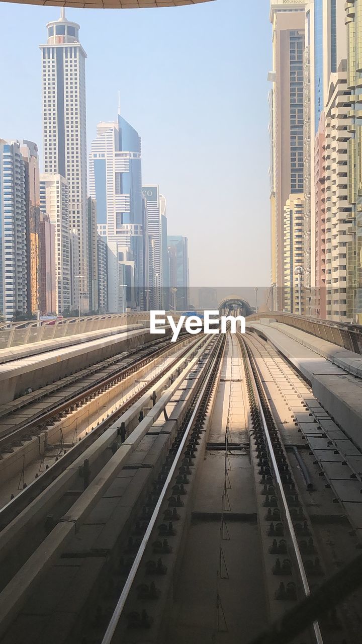 RAILROAD TRACKS BY BUILDINGS AGAINST SKY IN CITY