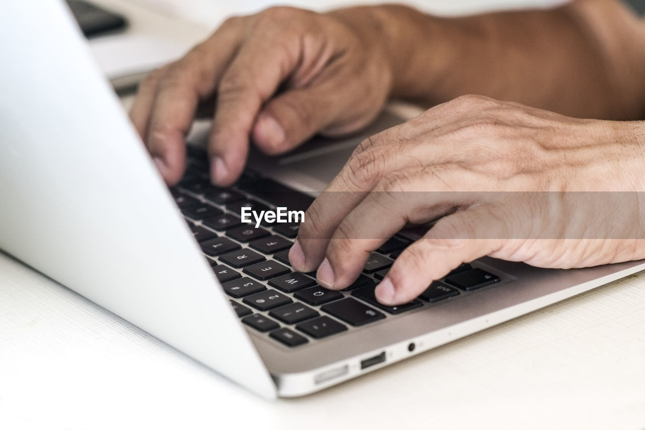 Cropped image of hands using laptop at table