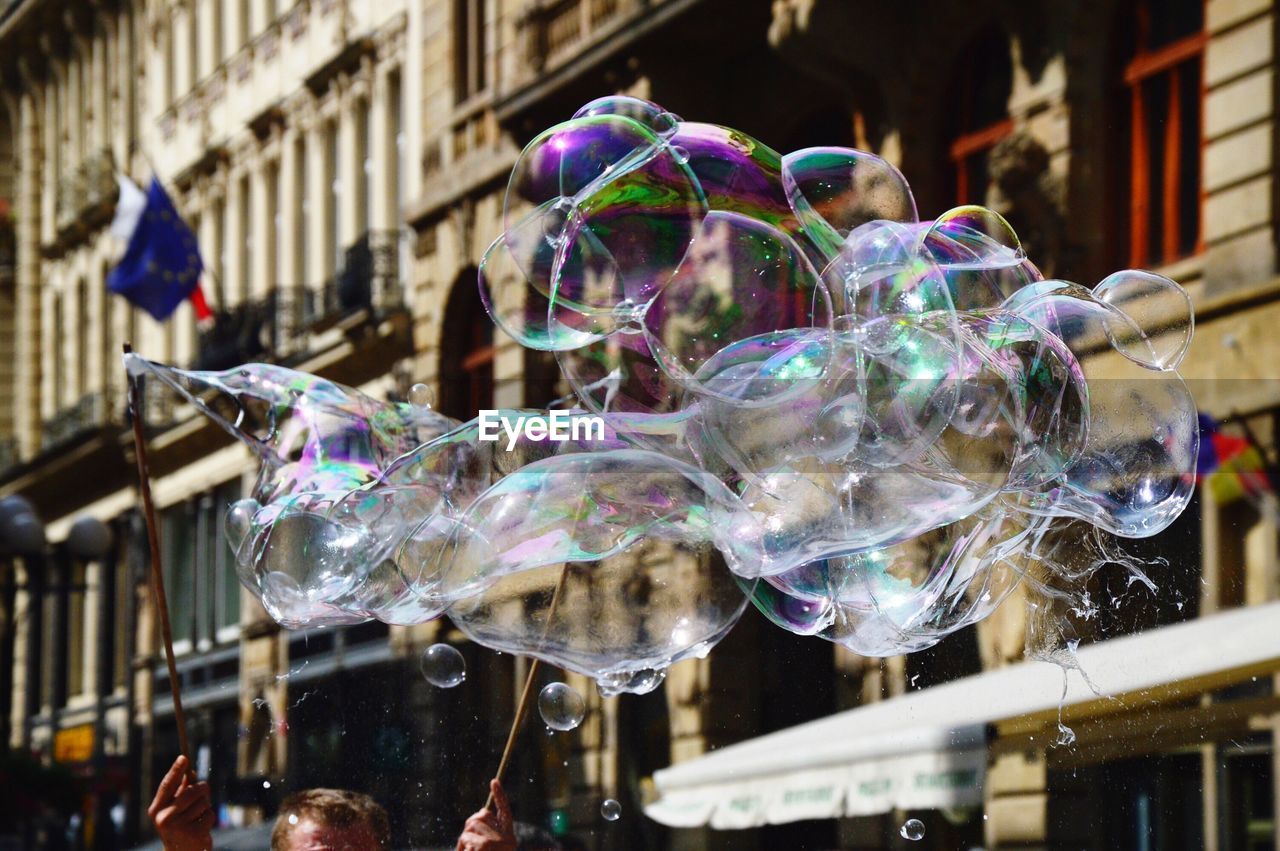 Cropped image of man making bubbles against buildings